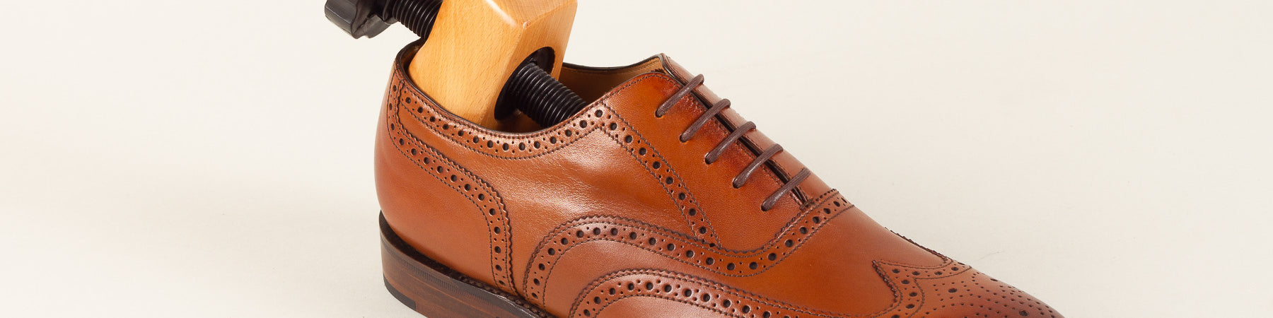 Close-up of a brown leather wingtip shoe with a wooden shoe stretcher, conveying a helpful and practical tone.