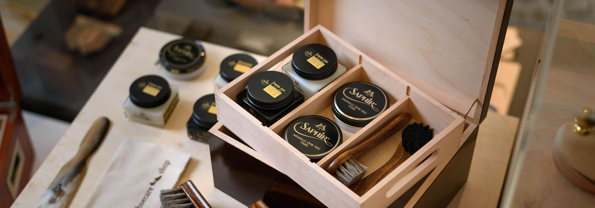 An open wooden box with Saphir shoe polish and brushes, evoking a sense of luxurious shoe care and sophisticated grooming.