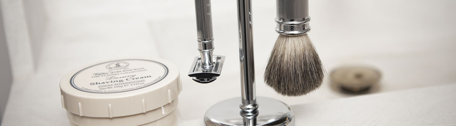 A luxurious wet shaving setup with a badger brush, safety razor on a stand, and Taylor of Old Bond Street shaving cream.