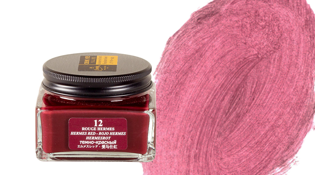 A glass jar of Rouge Hermès ink, labeled “12 Hermes Red,” sits next to a large swatch of the deep pink-red ink brushed onto a white background.
