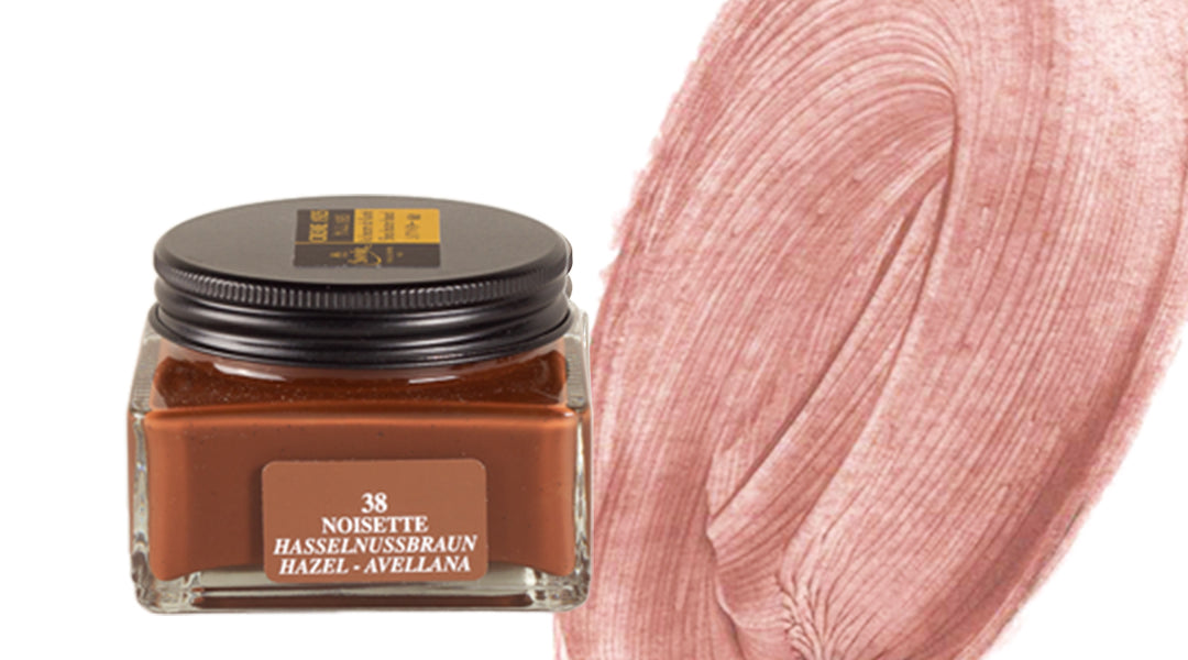 A square glass jar of brown paint labeled NOISETTE HASSELNUSS BRAUN HAZEL-AVELLANA 38 next to a textured smear of light brown or hazel-colored paint on a white background.